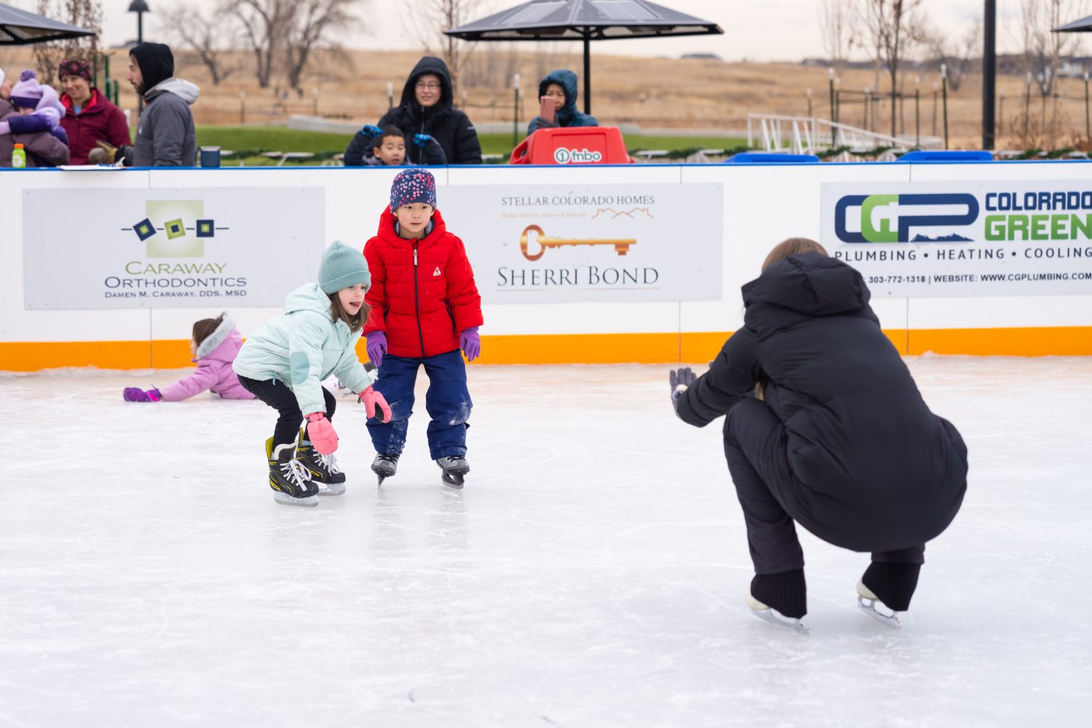 Skating coach instructing two young skaters how to balance and catch themselves before they fall.
